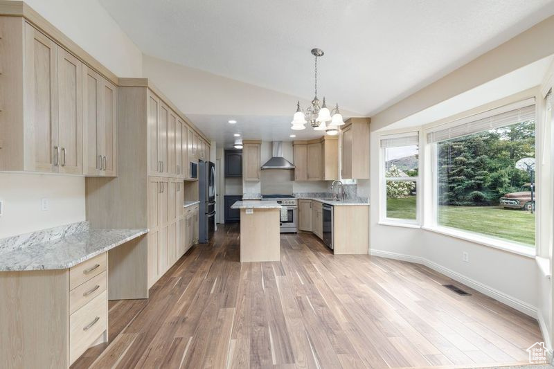 Kitchen featuring appliances with stainless steel finishes, wall chimney range hood, vaulted ceiling, light wood-style flooring, and light brown cabinets