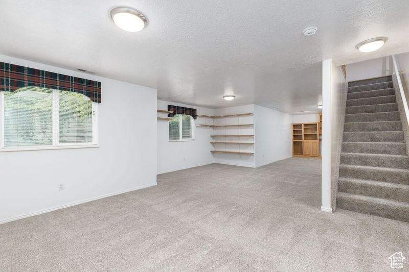 Unfurnished living room featuring carpet, stairway, a textured ceiling, and baseboards