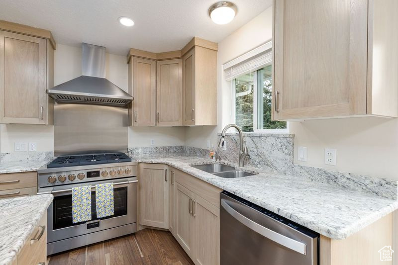 Kitchen with stainless steel appliances, wall chimney range hood, a sink, light brown cabinetry, and recessed lighting