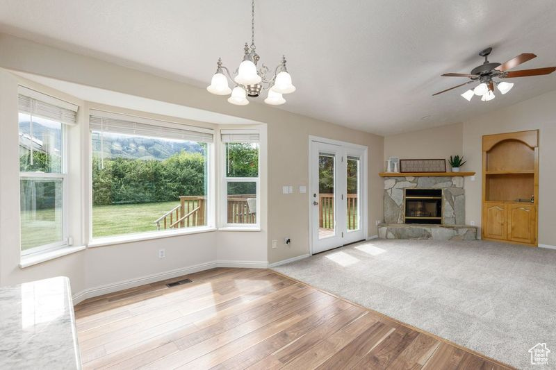 Unfurnished living room featuring light wood finished floors, healthy amount of natural light, a stone fireplace, baseboards, and vaulted ceiling