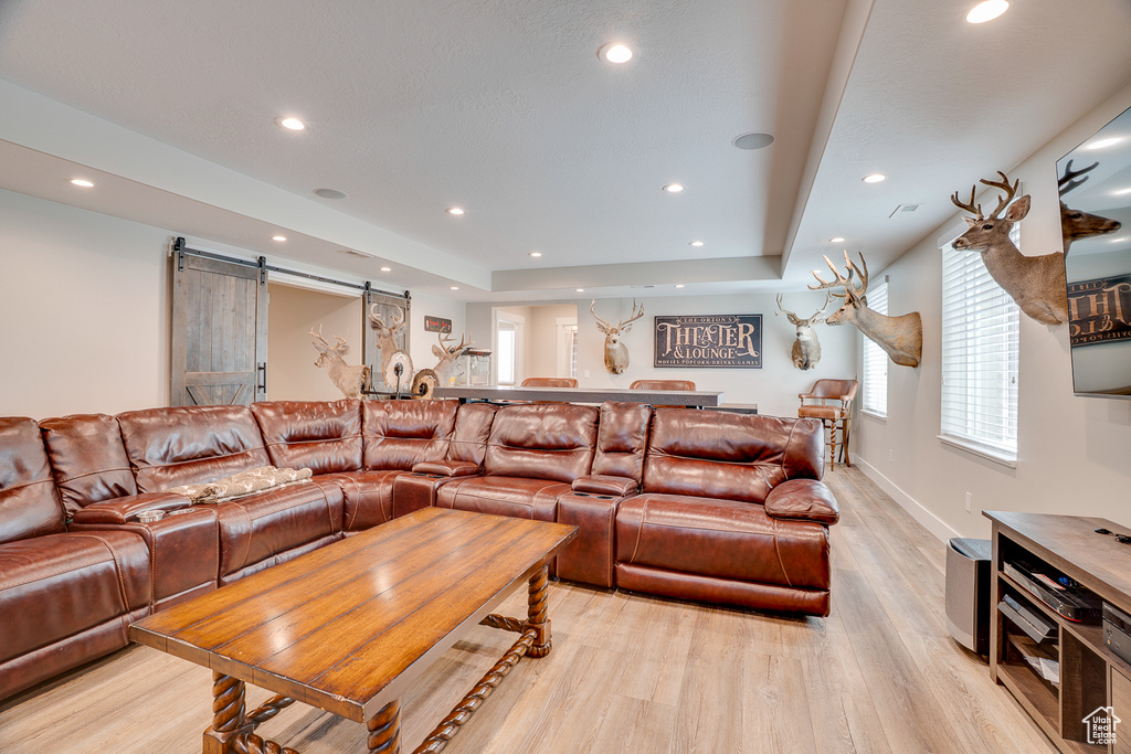 Living room featuring a barn door, light wood finished floors, recessed lighting, a tray ceiling, and baseboards