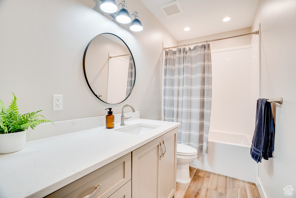 Full bath featuring wood finished floors, vanity, toilet, shower / tub combo with curtain, and recessed lighting