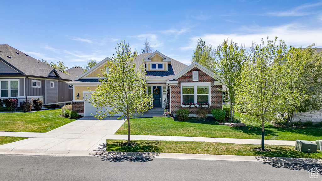 Craftsman-style house with brick siding, an attached garage, a front yard, and driveway