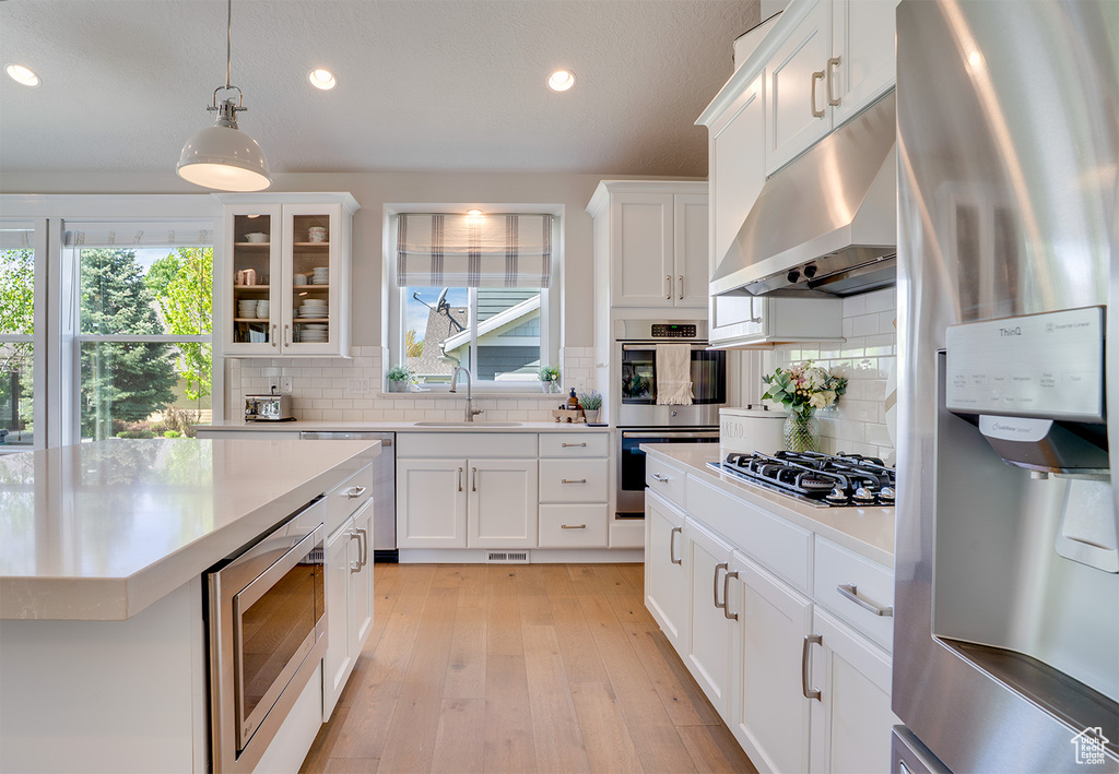 Kitchen with stainless steel appliances, under cabinet range hood, a sink, light countertops, and recessed lighting