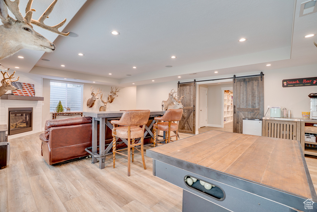 Game room featuring a barn door, a tray ceiling, light wood-style floors, recessed lighting, and a fireplace