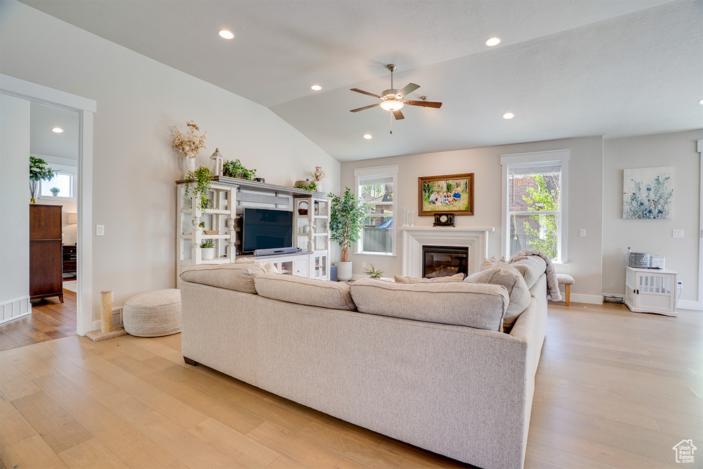 Living room with light wood-style flooring, ceiling fan, a glass covered fireplace, recessed lighting, and vaulted ceiling