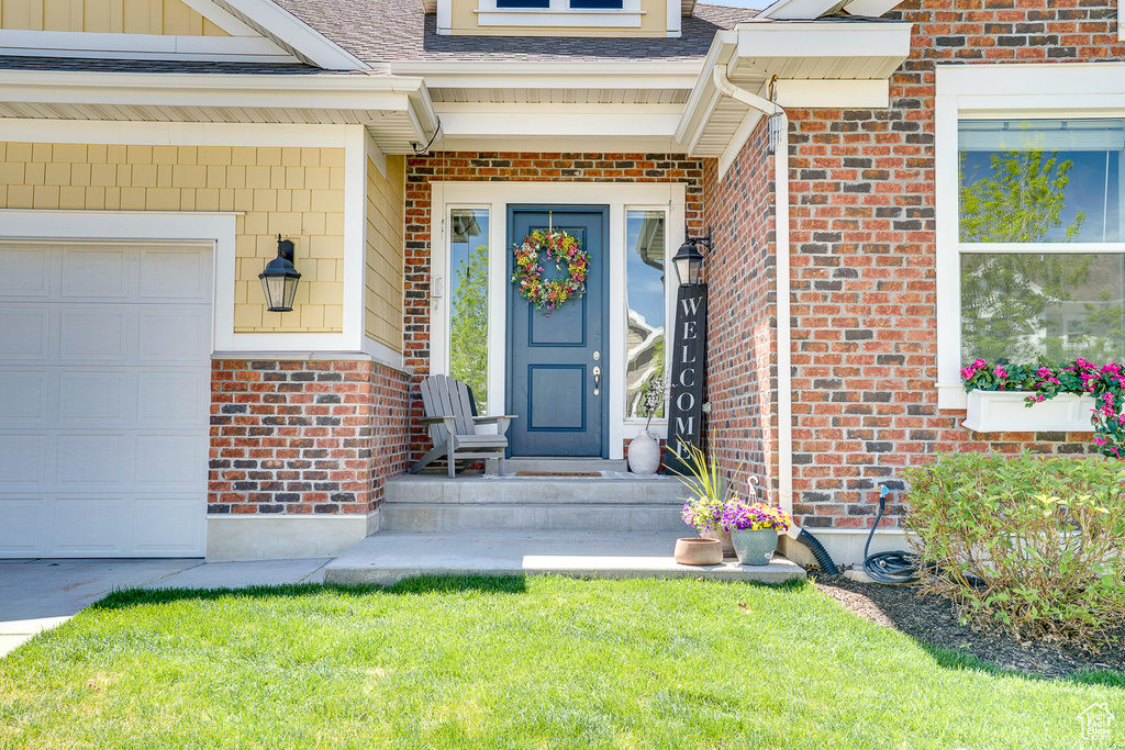 Property entrance featuring brick siding, a shingled roof, and an attached garage