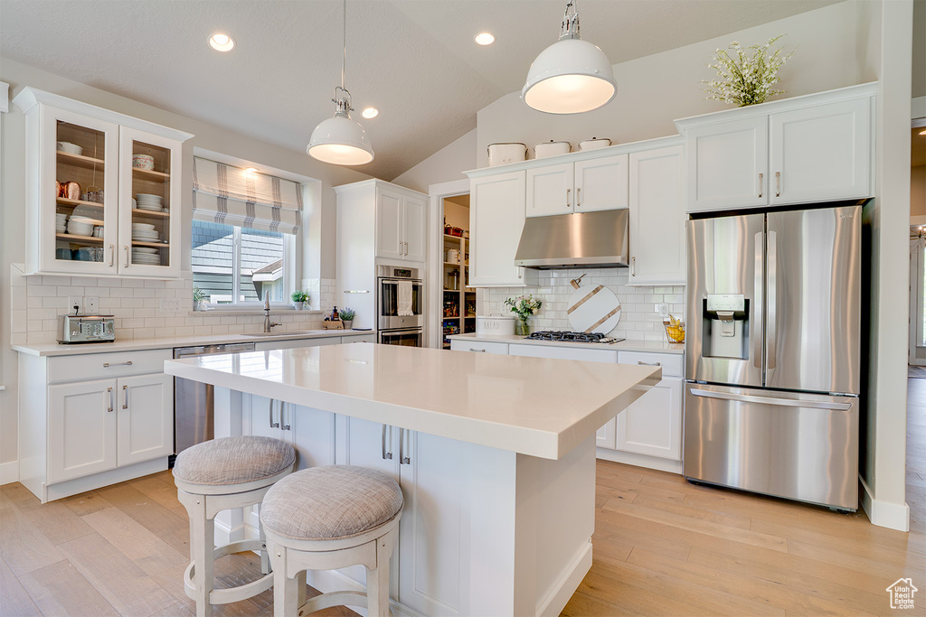 Kitchen featuring appliances with stainless steel finishes, under cabinet range hood, a sink, a center island, and white cabinets