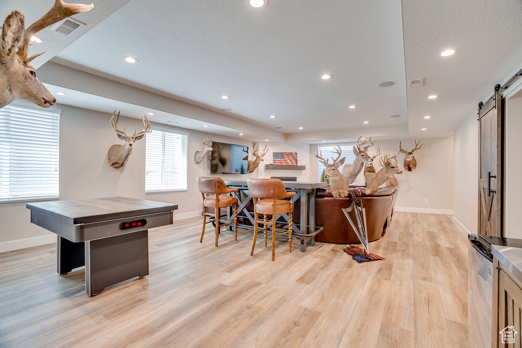 Rec room featuring a barn door, baseboards, light wood-style floors, plenty of natural light, and recessed lighting