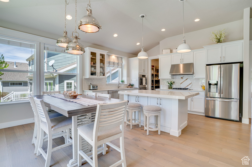Kitchen with appliances with stainless steel finishes, under cabinet range hood, a center island, light countertops, and decorative backsplash