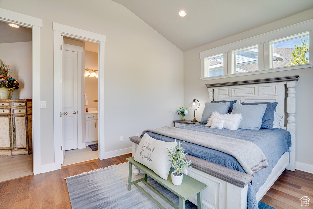 Bedroom with lofted ceiling, wood finished floors, baseboards, recessed lighting, and ensuite bathroom