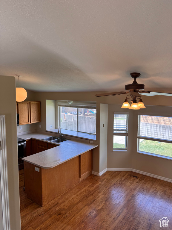 Kitchen featuring a sink, a peninsula, wood finished floors, ceiling fan, and brown cabinetry