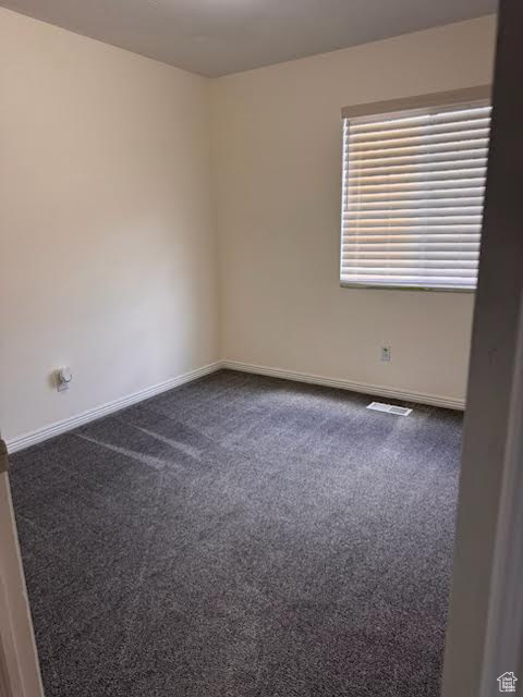 Spare room featuring dark carpet and baseboards
