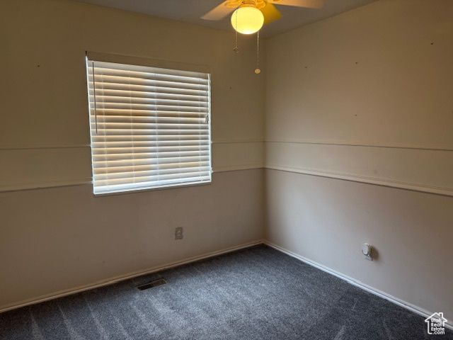 Spare room featuring a ceiling fan, dark colored carpet, and healthy amount of natural light