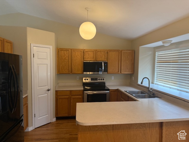 Kitchen with appliances with stainless steel finishes, a sink, light countertops, wood finished floors, and lofted ceiling