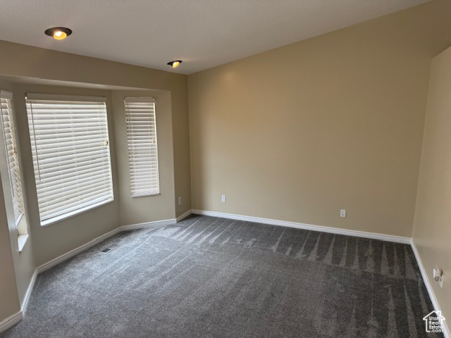 Unfurnished room featuring dark colored carpet, baseboards, and healthy amount of natural light
