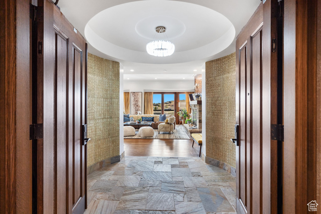 Hallway with light stone finish flooring, a chandelier, and a tray ceiling