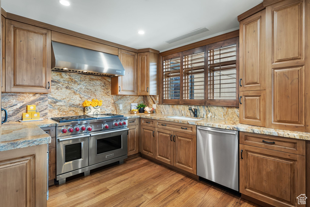 Kitchen featuring stainless steel appliances, wall chimney range hood, a sink, tasteful backsplash, and light wood-style flooring