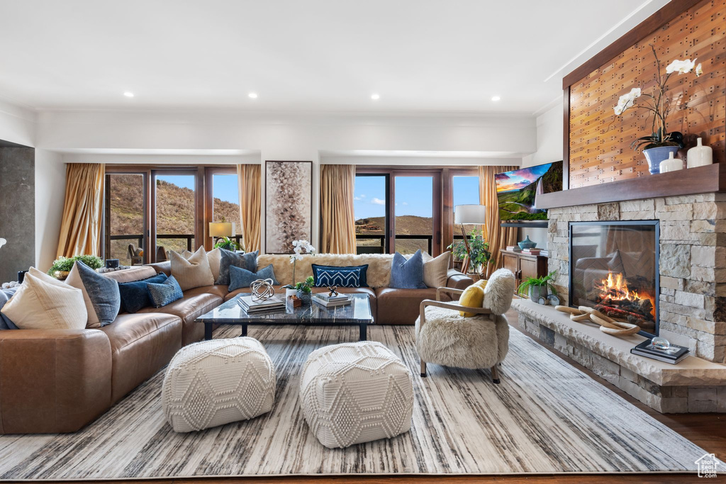 Living area with a stone fireplace, wood finished floors, ornamental molding, and recessed lighting