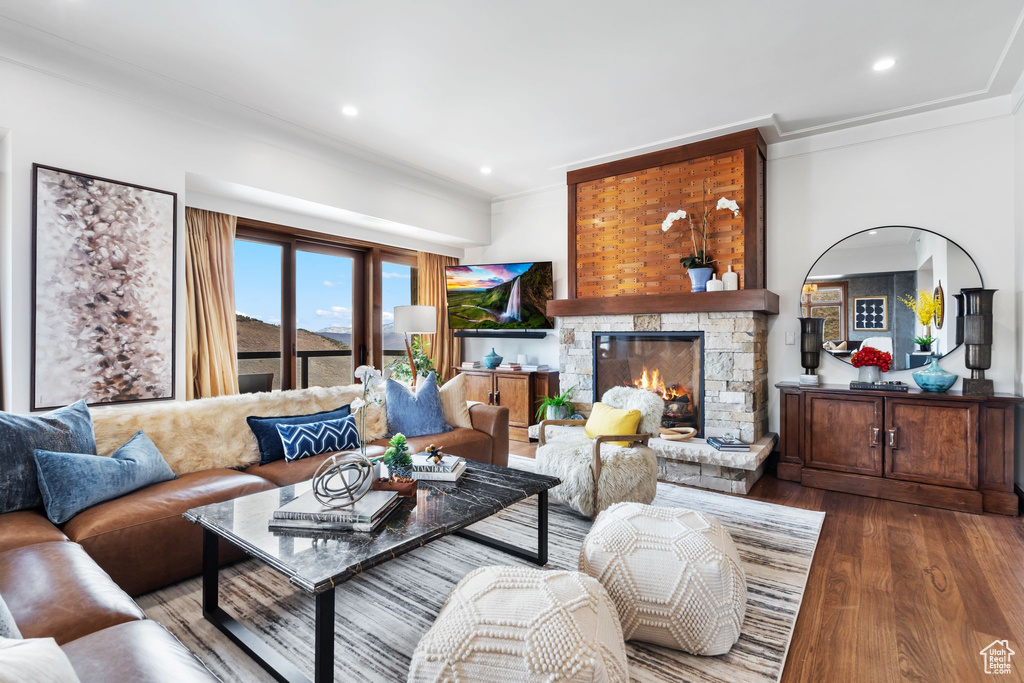 Living room featuring crown molding, wood finished floors, a stone fireplace, and recessed lighting