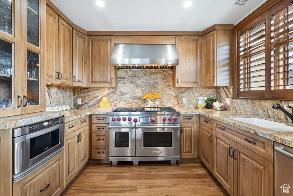 Kitchen featuring appliances with stainless steel finishes, wall chimney exhaust hood, a sink, light stone countertops, and backsplash