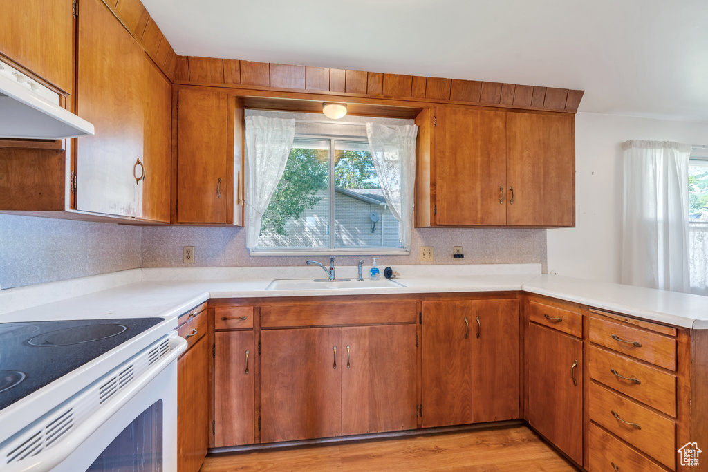 Kitchen with extractor fan, light countertops, a peninsula, brown cabinets, and electric range