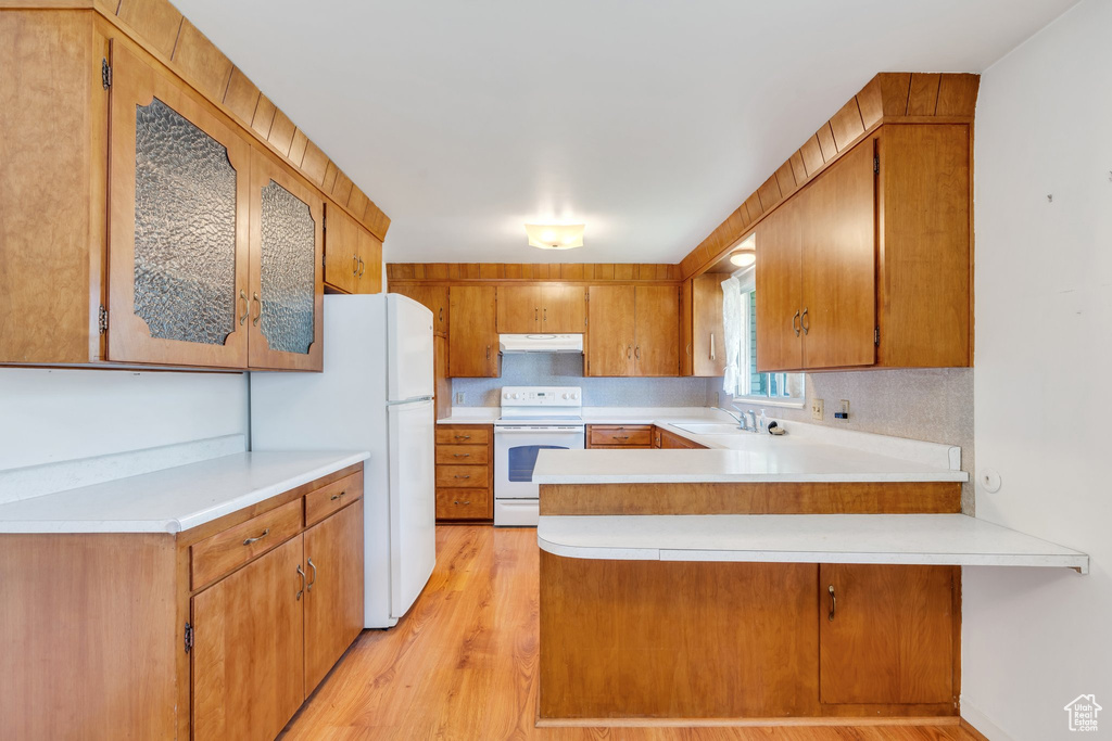 Kitchen with white appliances, under cabinet range hood, a sink, a peninsula, and light countertops