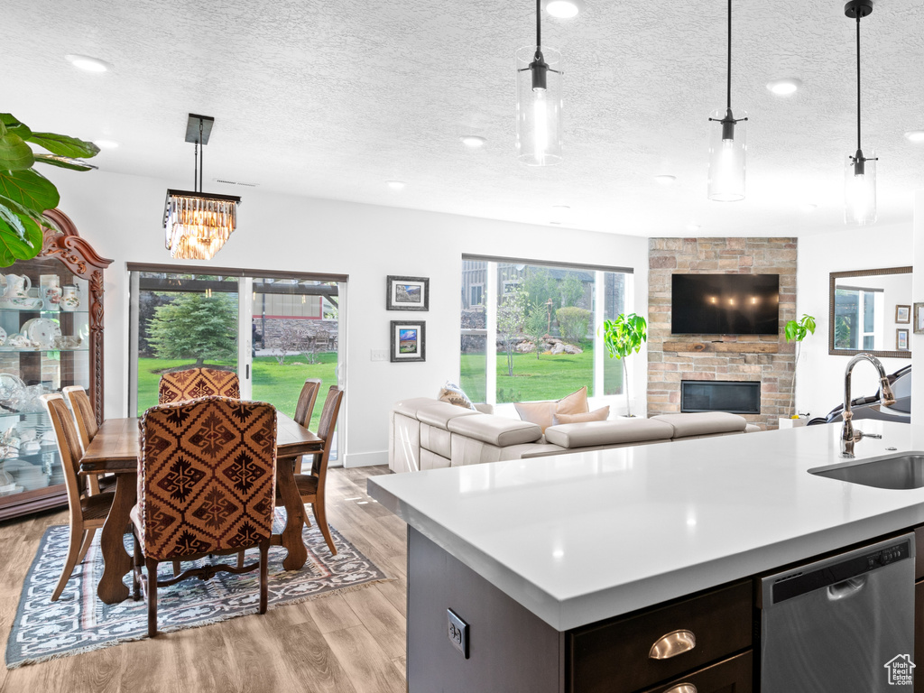 Kitchen with dishwasher, a sink, a fireplace, light wood-style floors, and light countertops