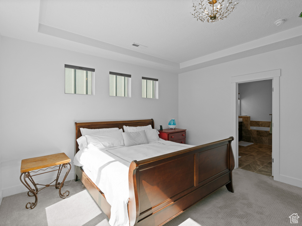 Carpeted bedroom featuring a tray ceiling, a chandelier, and connected bathroom