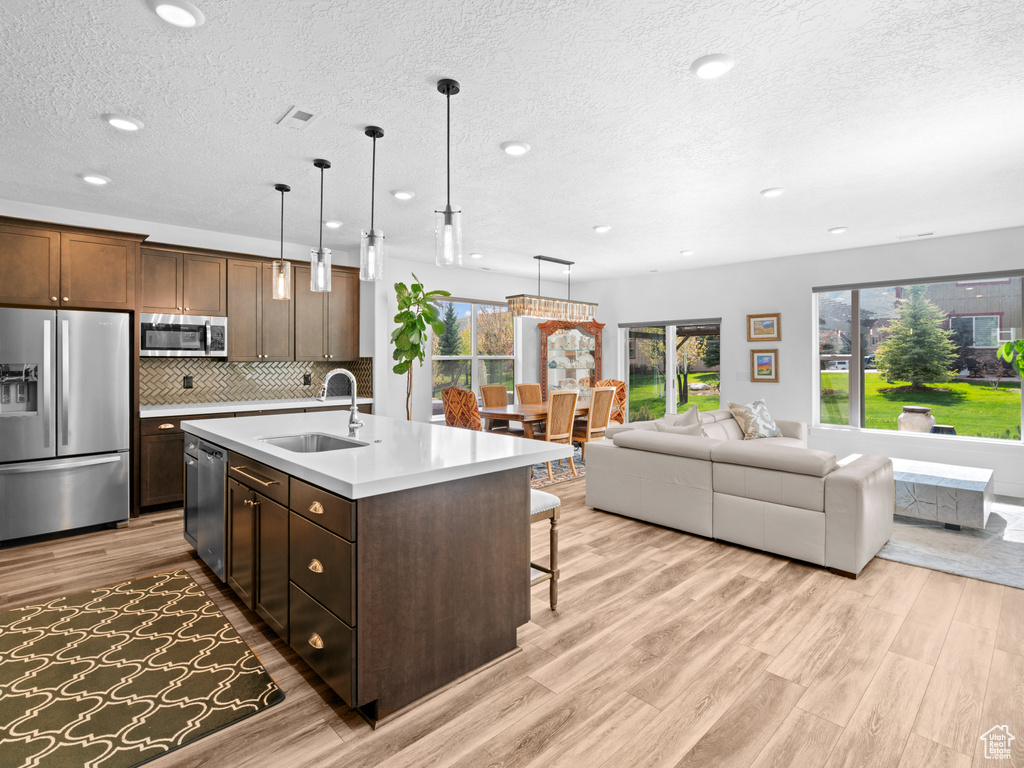 Kitchen featuring appliances with stainless steel finishes, a sink, a textured ceiling, light wood finished floors, and light countertops