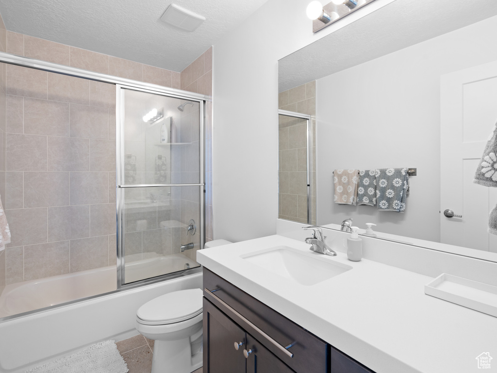 Full bathroom featuring toilet, shower / bath combination with glass door, vanity, tile patterned flooring, and a textured ceiling