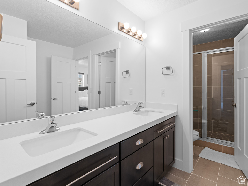 Full bathroom with a stall shower, double vanity, ensuite bathroom, tile patterned floors, and toilet