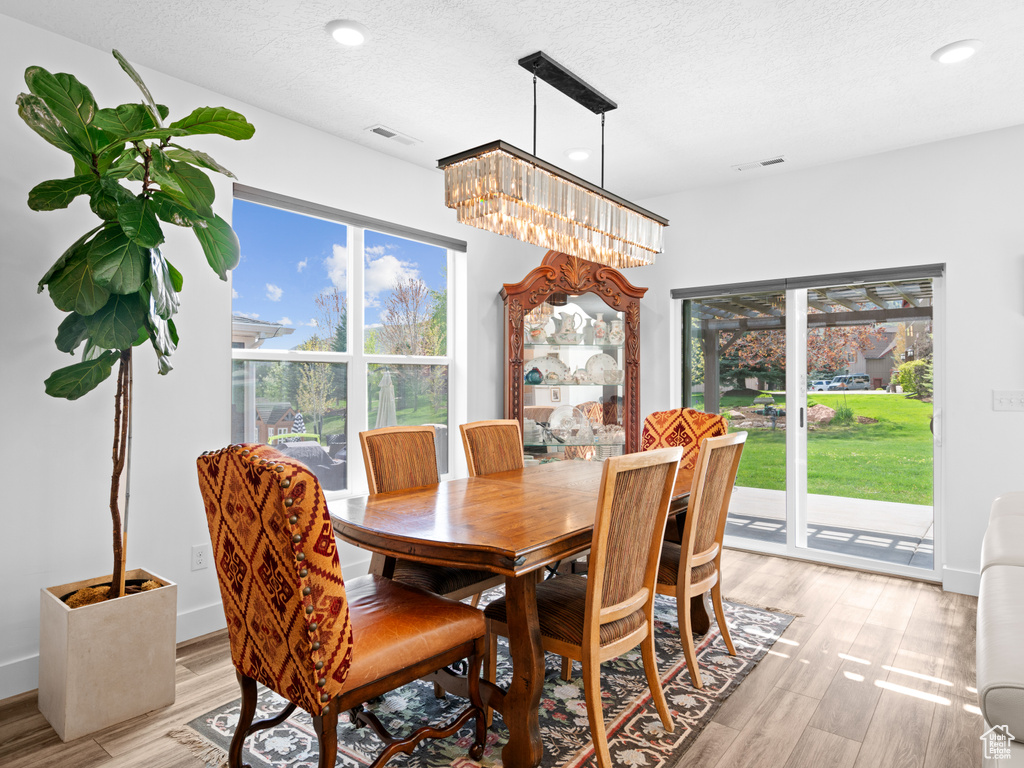 Dining area with a chandelier, recessed lighting, light wood-type flooring, and a textured ceiling