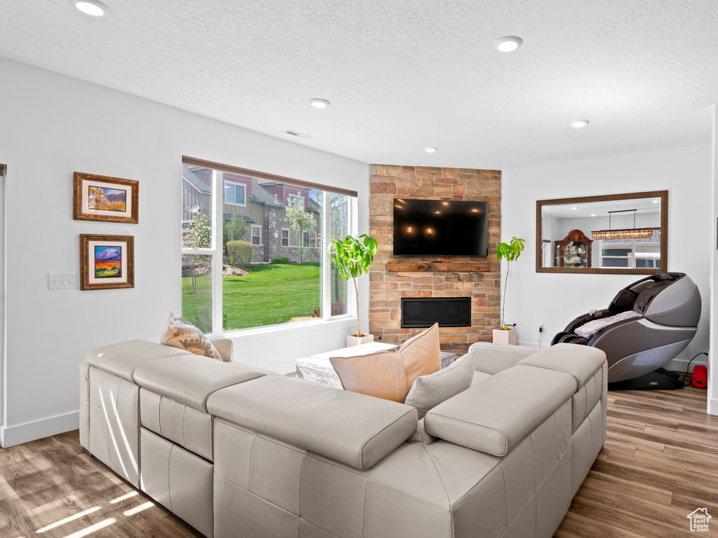 Living room featuring wood finished floors, a fireplace, baseboards, a textured ceiling, and recessed lighting