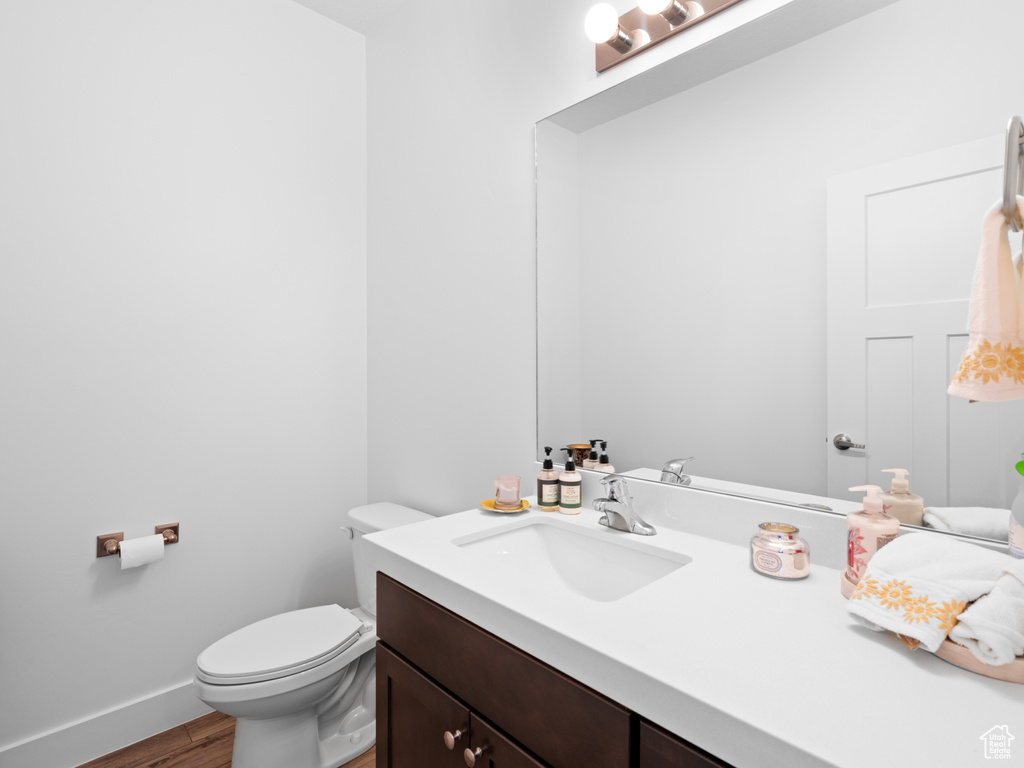 Half bath featuring wood finished floors, toilet, vanity, and baseboards