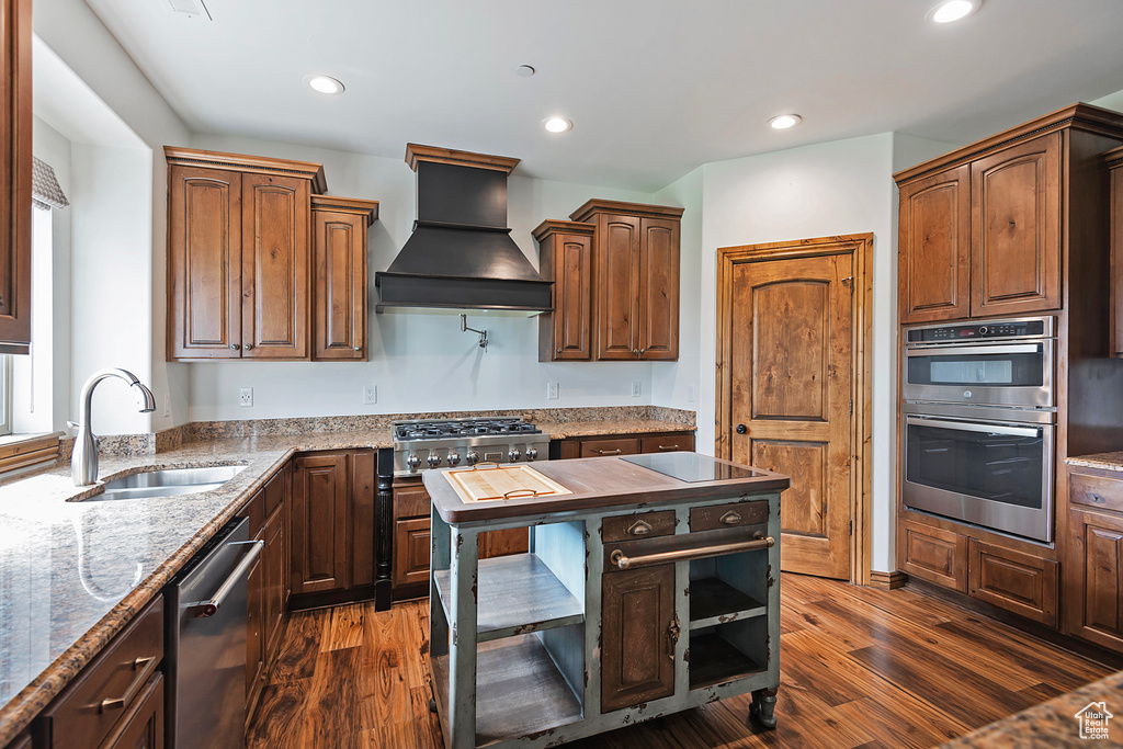 Kitchen featuring premium range hood, appliances with stainless steel finishes, a sink, dark wood finished floors, and recessed lighting