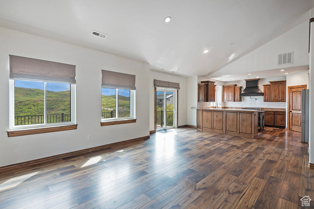 Kitchen with custom range hood, range, a peninsula, dark wood-style floors, and high vaulted ceiling