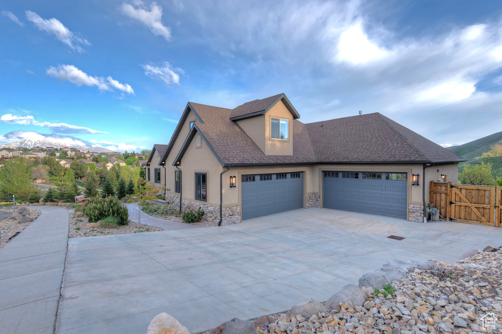 View of front facade with stone siding, stucco siding, an attached garage, driveway, and a gate