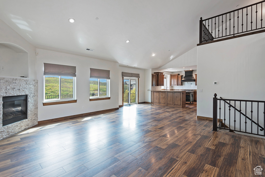 Unfurnished living room with a stone fireplace, dark wood-type flooring, recessed lighting, baseboards, and high vaulted ceiling