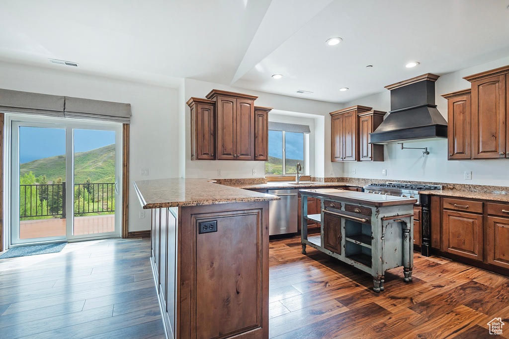 Kitchen with custom exhaust hood, appliances with stainless steel finishes, a peninsula, dark wood finished floors, and recessed lighting