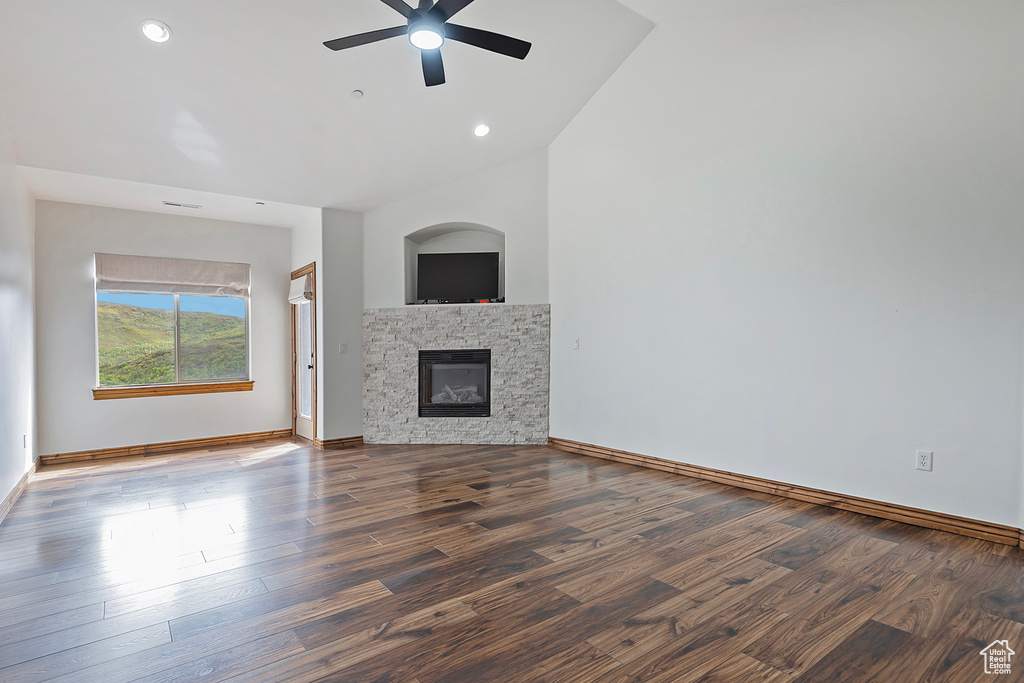 Unfurnished living room with ceiling fan, wood finished floors, a stone fireplace, vaulted ceiling, and baseboards