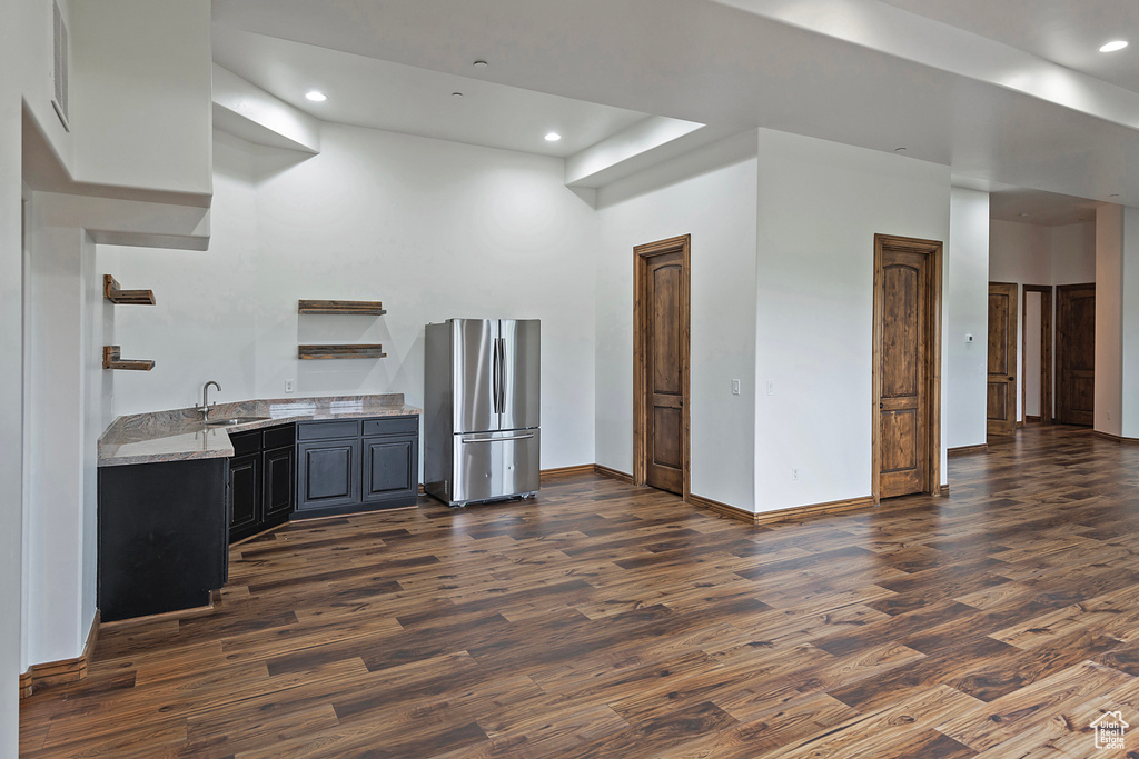 Kitchen featuring freestanding refrigerator, a sink, dark wood-type flooring, baseboards, and light stone counters