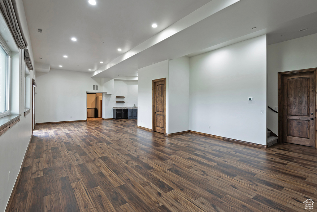 Unfurnished living room with recessed lighting, dark wood finished floors, stairs, and baseboards