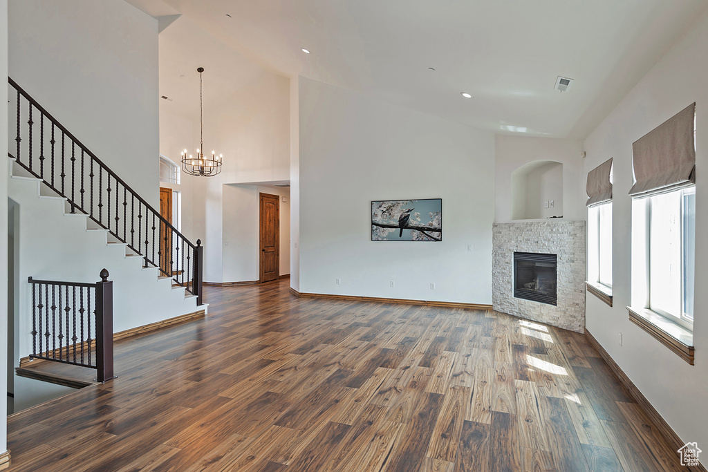Unfurnished living room with wood finished floors, a fireplace, a chandelier, high vaulted ceiling, and baseboards