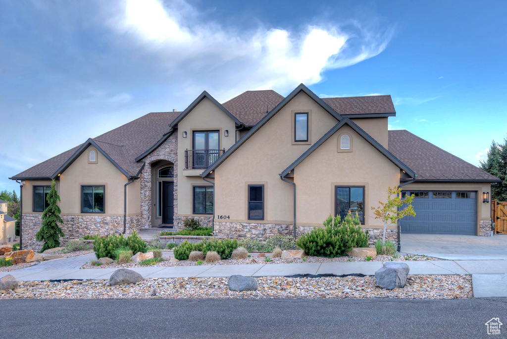 French country style house with a balcony, stone siding, stucco siding, and concrete driveway