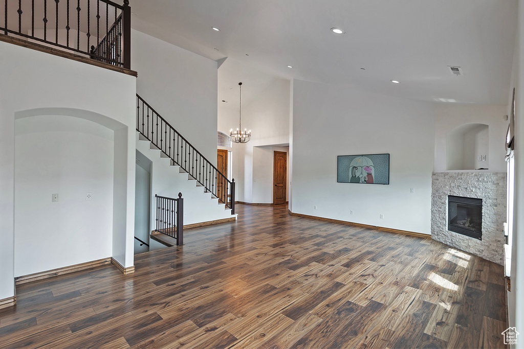 Unfurnished living room with wood finished floors, a stone fireplace, stairway, high vaulted ceiling, and baseboards