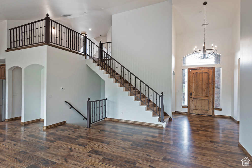 Foyer with a high ceiling, wood finished floors, arched walkways, a chandelier, and baseboards