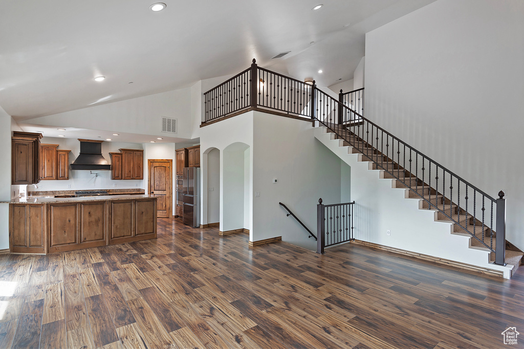 Kitchen with custom exhaust hood, a peninsula, freestanding refrigerator, arched walkways, and dark wood-type flooring
