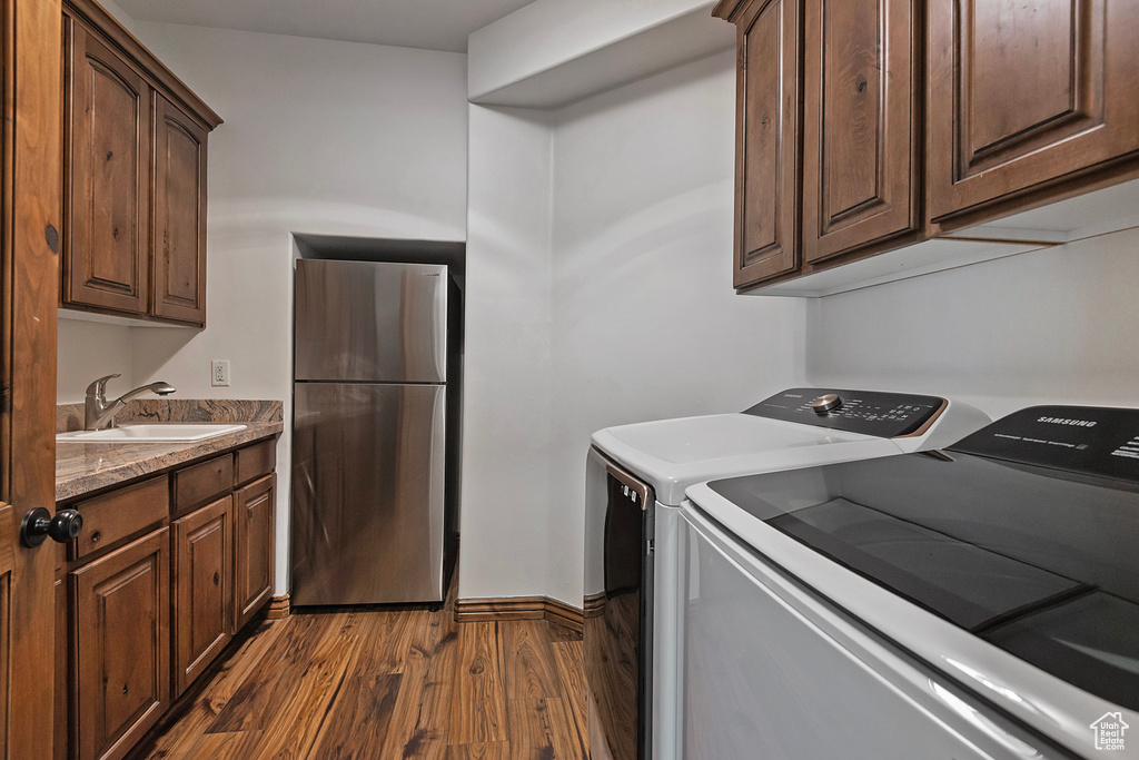 Clothes washing area featuring dark wood-style floors, washer and clothes dryer, and cabinet space
