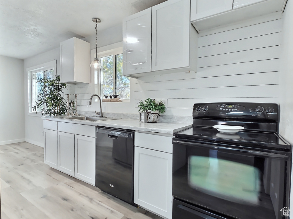 Kitchen featuring black appliances, a sink, light wood-type flooring, white cabinetry, and baseboards